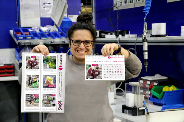Una trabajadora, sonriente, muestra en una mano un calendario, y en otra, un cartel de la campaña.